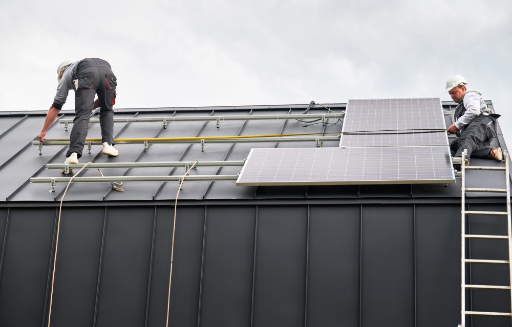Men measuring photovoltaic solar panels with tape measure. Technicians taking measurements before mounting solar modules on roof of house for generating electricity through photovoltaic effect.